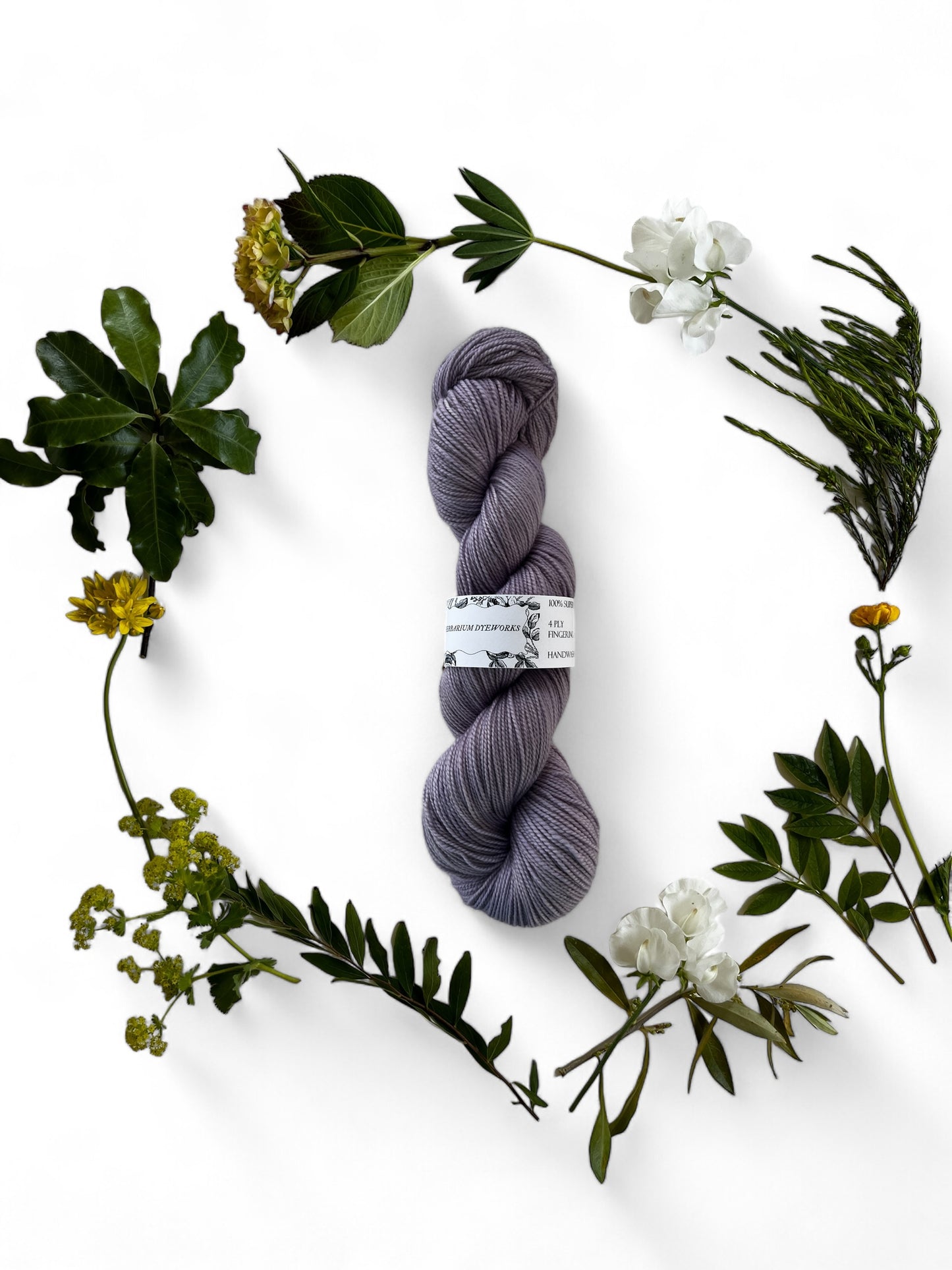One skein of merino yarn in lilac purple dyed with Logwood and surrounded by a wreath of flowers and leaves