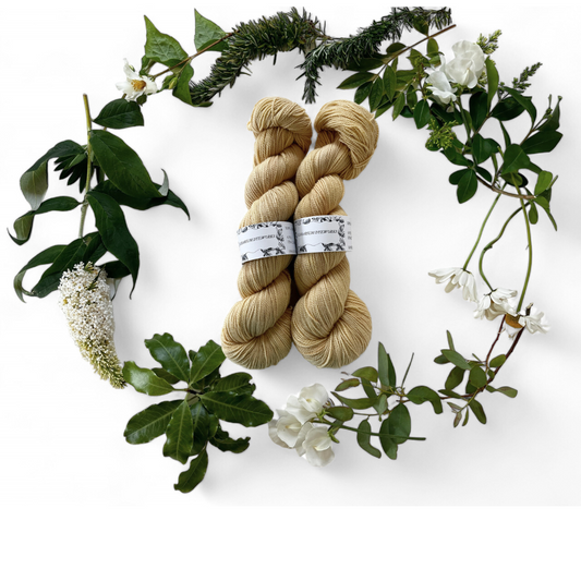 Two skeins of merino yarn in straw yellow dyed with Rhubarb Root and surrounded by a wreath of flowers and leaves