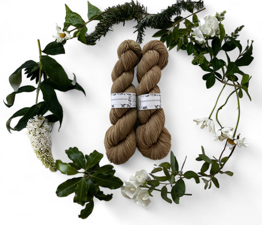 Two skeins of merino yarn in olive tan dyed with Indigo and Chrolophyllin and surrounded by a wreath of flowers and leaves