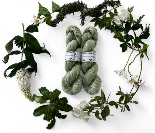 Two skeins of merino yarn in tea green dyed with Chrolophyllin and surrounded by a wreath of flowers and leaves