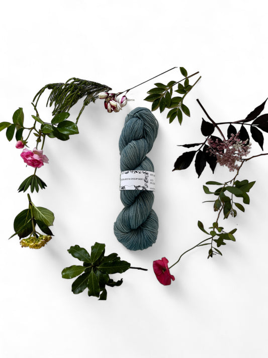 One skein of merino yarn in Swedish blue dyed with Indigo and surrounded by a wreath of flowers and leaves