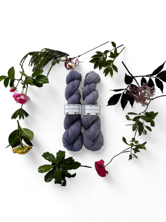 Two skeins of merino yarn in mid-purple dyed with Logwood and surrounded by a wreath of flowers and leaves