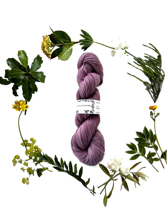 One skein of merino yarn in pink-purple dyed with Lac and Logwood and surrounded by a wreath of flowers and leaves