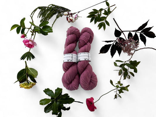 Two skeins of merino yarn in mulberry pink dyed with Lac and surrounded by a wreath of flowers and leaves