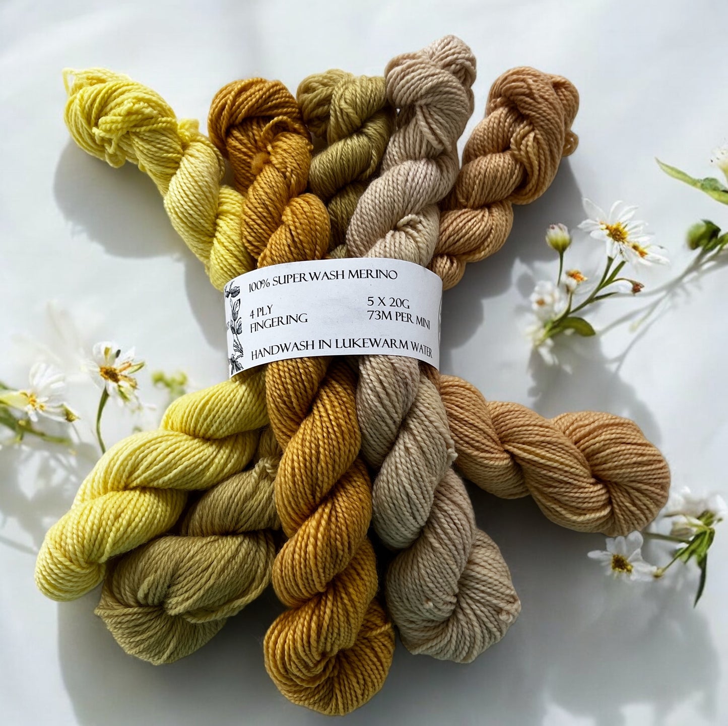 Five naturally dyed mini skeins of merino in lemon, yellow-green, golden mustard, pinky sand and pale apricot yellow held together with a yarn band