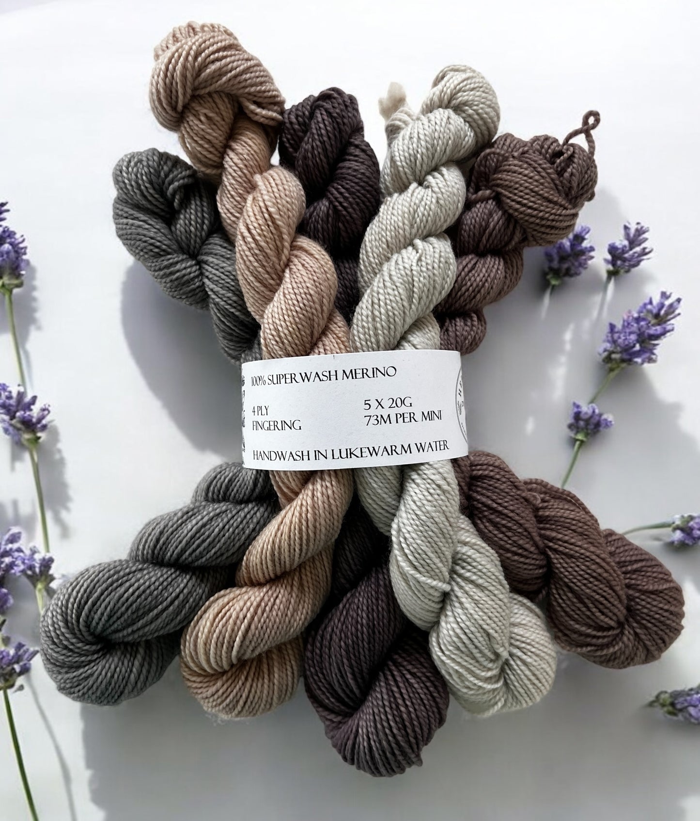 Five mini skeins of naturally dyed merino in slate grey, oyster grey-pink, plum grey, pale silver and taupe held together with a yarn band