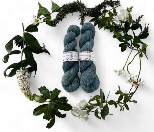 Two skeins of merino yarn in denim blue dyed with Indigo and surrounded by a wreath of flowers and leaves