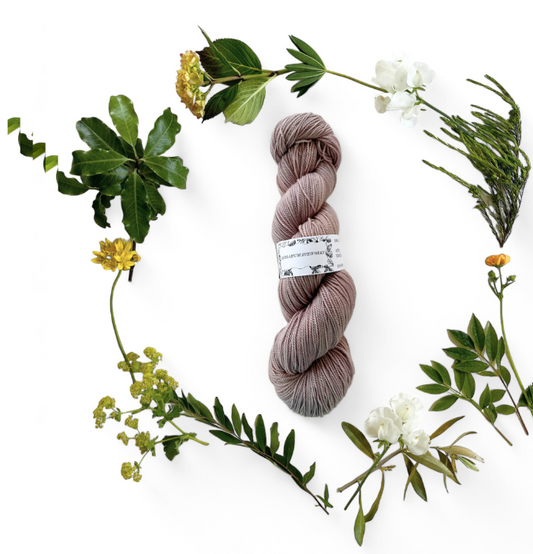 One skein of merino yarn in pale purple-grey-beige dyed with Logwood and Coreopsis and surrounded by a wreath of flowers and leaves